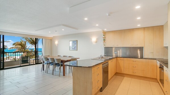A modern kitchen with a central island, wooden cabinets, and a view of the ocean. - Rocks Resort 4G - Currumbin Beachfront - Min. 3 night stays! (Currumbin)