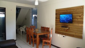 Een eethoek met een houten tafel en stoelen, een televisie bevestigd aan een houten wandpaneel en een plafondventilator.