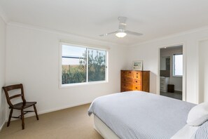 Une chambre à coucher avec un lit, une commode en bois, une chaise, une fenêtre et un ventilateur de plafond.