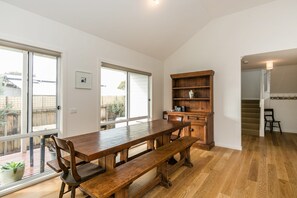 A spacious room with a large wooden dining table, a built-in bookshelf, and a staircase leading to an upper level.