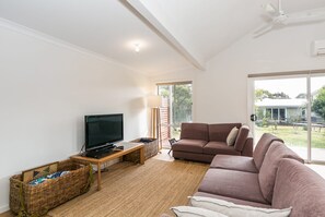 A modern living room with a flat-screen TV, a brown sofa, and a large window.