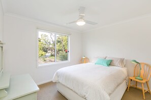 A bedroom with a bed, a window, a ceiling fan, and a desk.