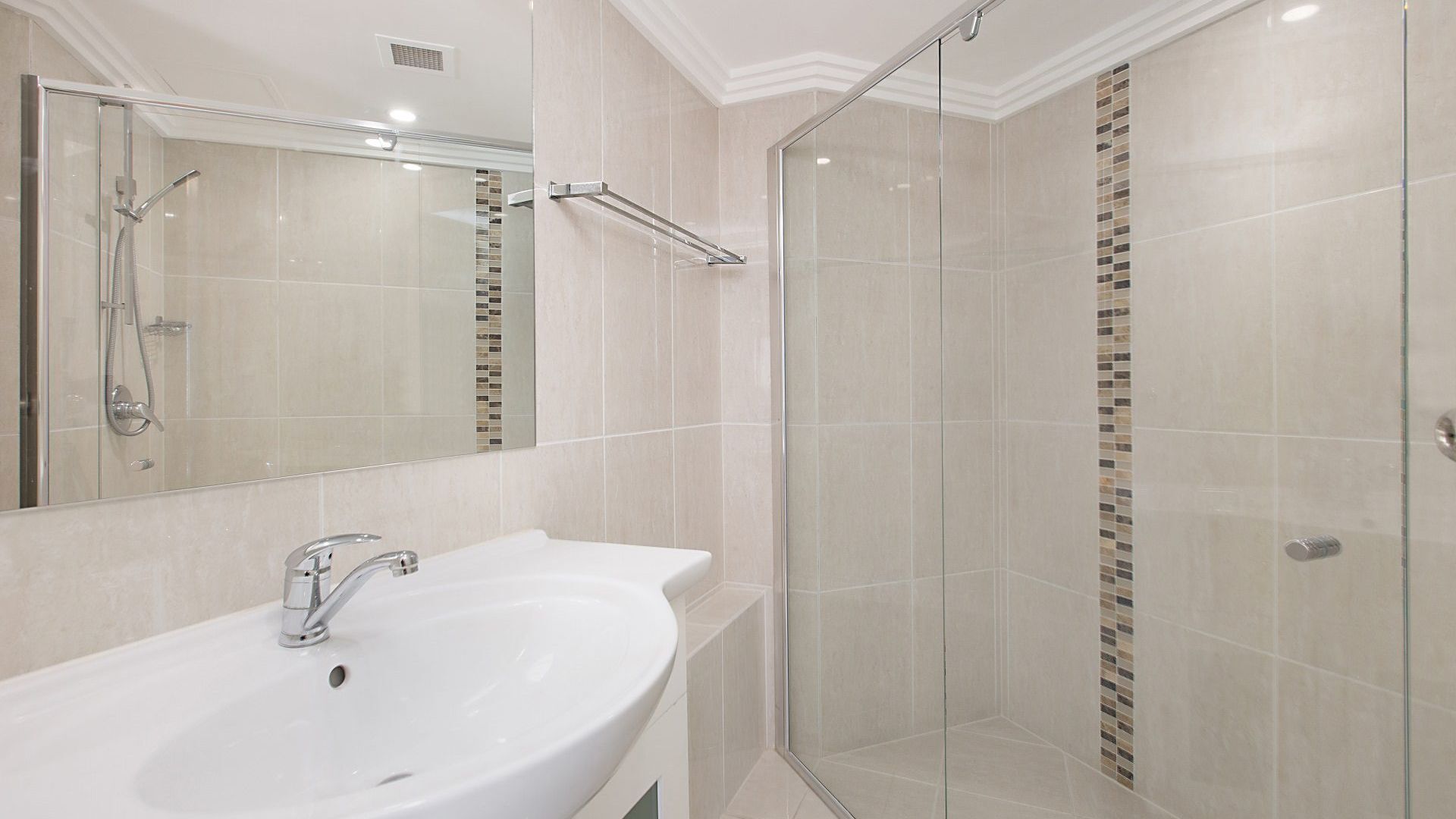 A modern bathroom with a large sink, a glass shower enclosure, and a tiled wall with a mosaic pattern.