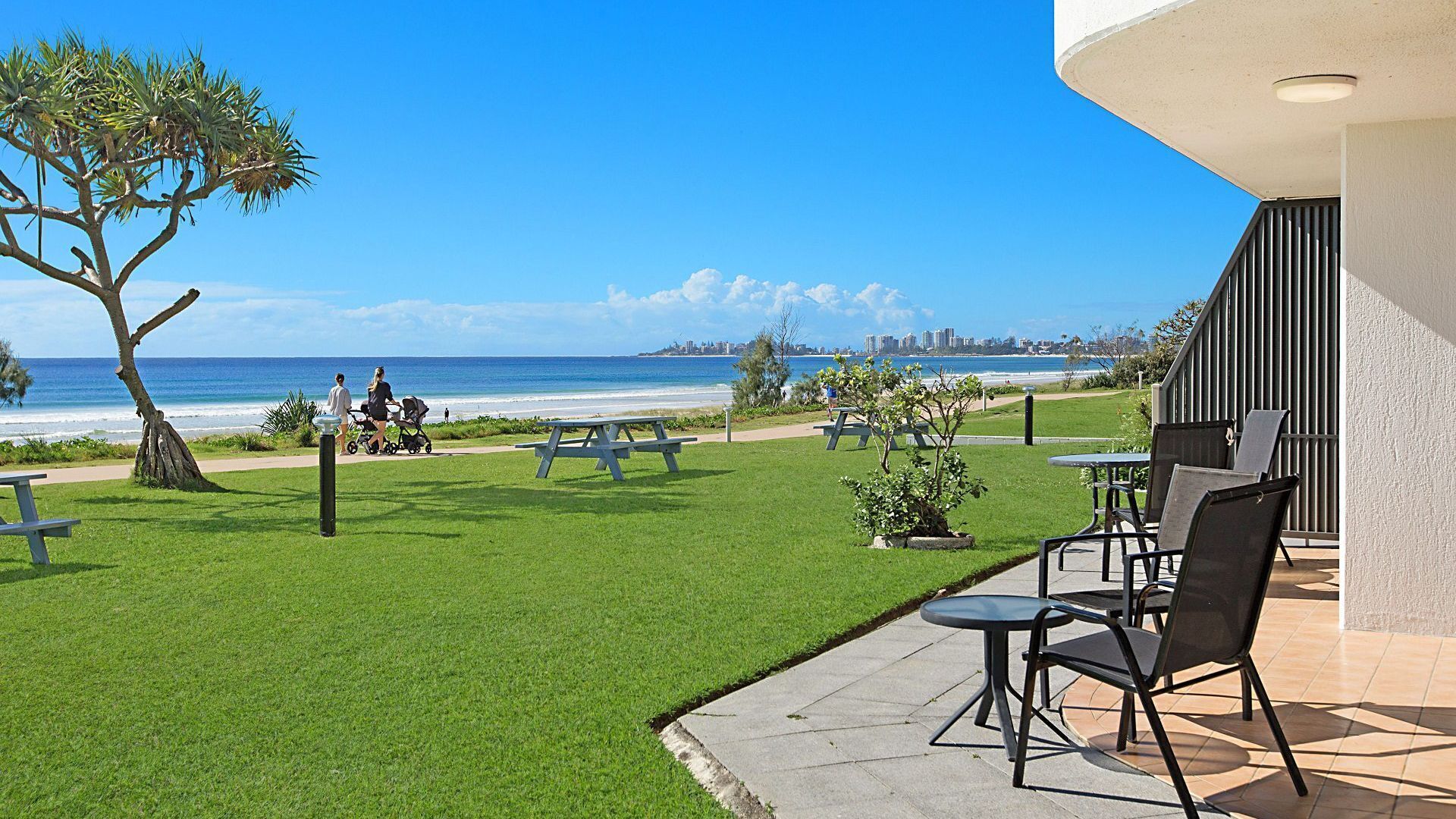 A patio with outdoor seating, a view of the beach, and a city skyline in the distance.
