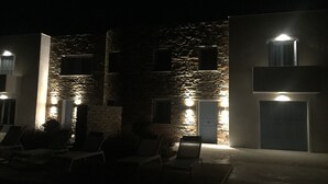 Un bâtiment aux murs de pierre et aux nombreuses fenêtres, dont certaines sont éclairées. Des fauteuils sont disposés à l’extérieur.