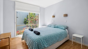 Une chambre à coucher avec un lit, une petite table blanche, une chaise en bois et une fenêtre donnant sur un paysage verdoyant.