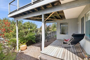 A covered outdoor patio with a wooden deck, a lounge chair, and a potted plant.