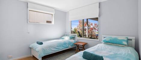 Une chambre avec deux lits, une fenêtre donnant sur des arbres, un luminaire au plafond et une petite table.