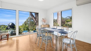 Un espace repas moderne avec une table en verre, des chaises en métal et une vue sur l’extérieur grâce à de grandes fenêtres.