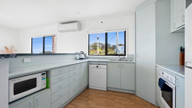 A modern kitchen with a dishwasher, oven, and a large window providing a view of the outdoors.