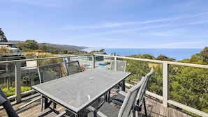 Une terrasse extérieure avec une table et des chaises en métal, offrant une vue sur un paysage côtier.