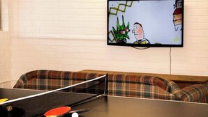 A ping pong table with a paddle and ball, a television displaying a cartoon, and a plaid sofa. - All Seasons—Coastal Charm Steps to Beach & Town (Dunsborough)