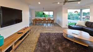 A modern living room with a flat-screen TV, a dining table with chairs, a sofa, a coffee table, and a ceiling fan. - All Seasons—Coastal Charm Steps to Beach & Town (Dunsborough)