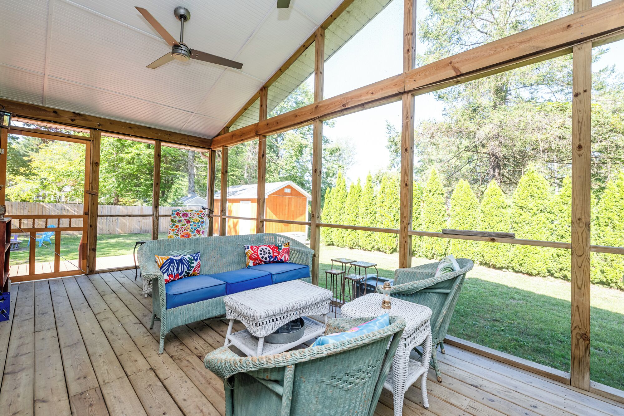 A covered patio with wicker furniture, large windows, and a ceiling fan.
