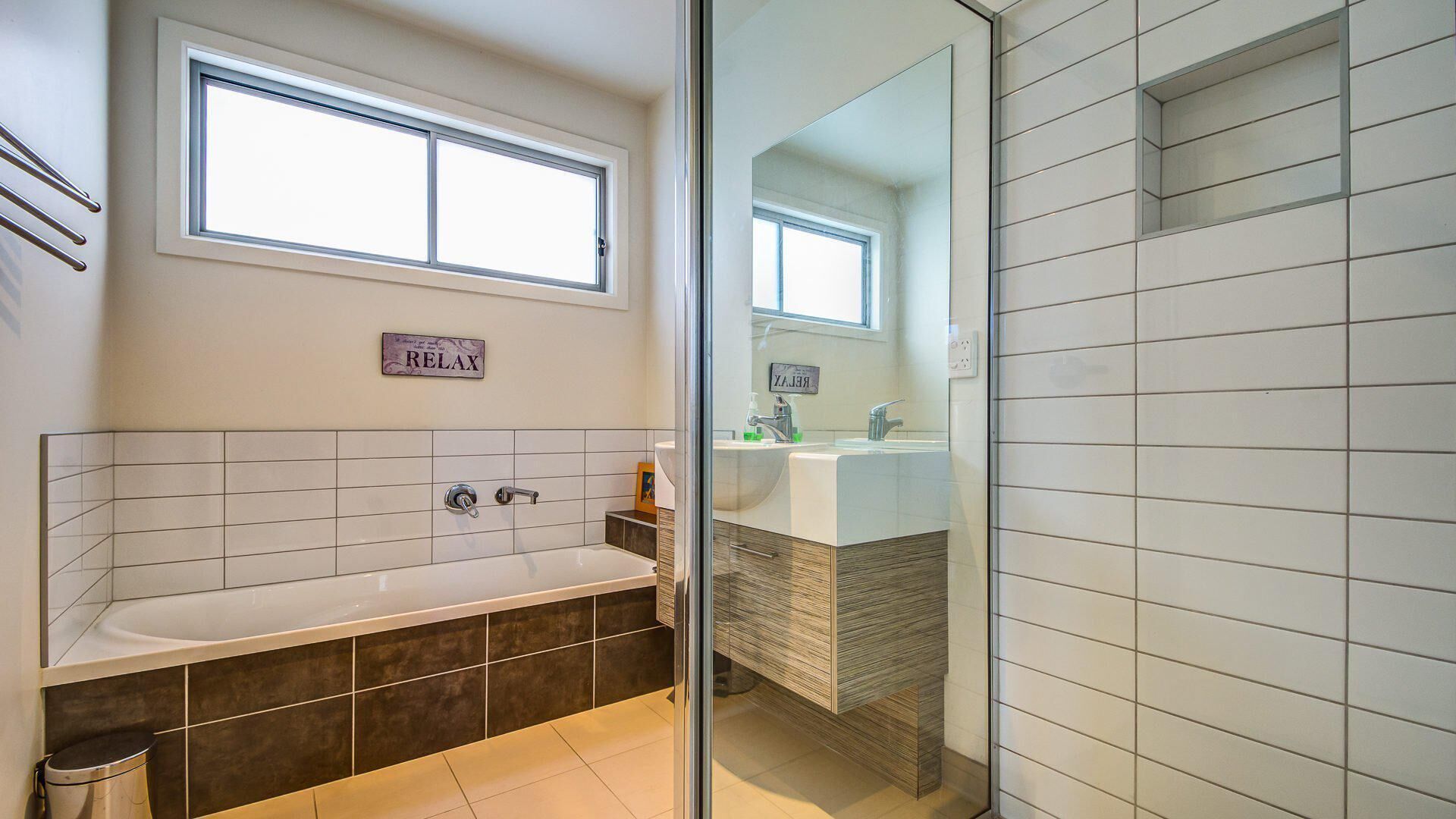 A modern bathroom with a bathtub, a large mirror, and a 'RELAX' sign.