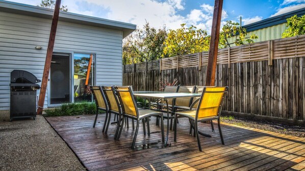 Une terrasse extérieure avec une table et des chaises, un barbecue et une clôture en bois.