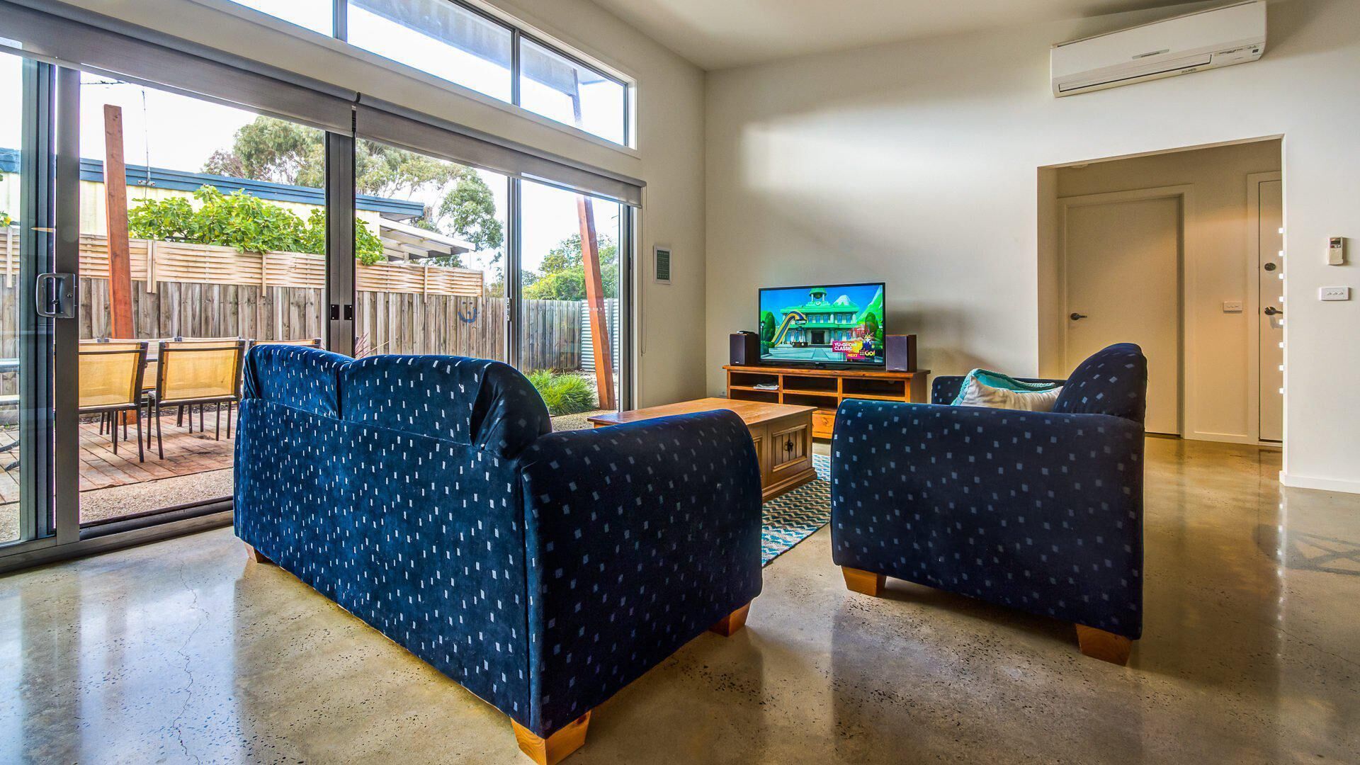 A living room with two blue patterned sofas, a wooden coffee table, and a flat-screen TV on a wooden stand.