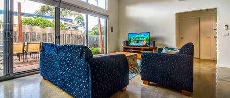 A living room with two blue patterned sofas, a wooden coffee table, and a flat-screen TV on a wooden stand.