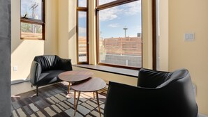 A modern room with large windows, a black leather sofa, a small round table, and a patterned rug.