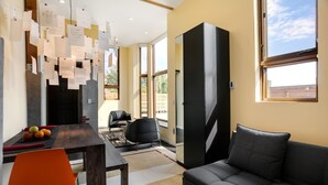 A modern living room with a sofa, a dining table with chairs, and a large window.