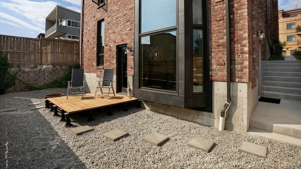 A modern building with a brick facade, large windows, and a wooden deck with steps leading to the entrance.