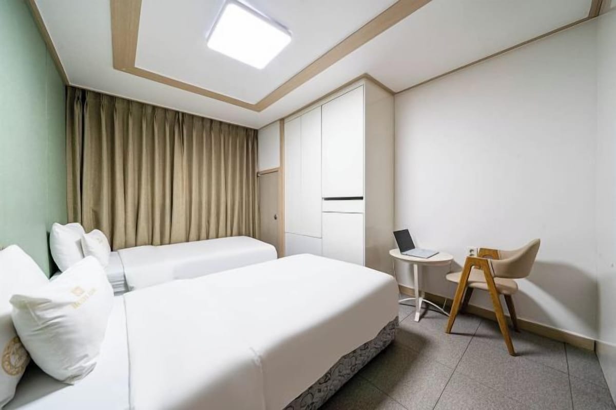 Une chambre d’hôtel avec deux lits, un bureau, une chaise et une fenêtre avec des rideaux.