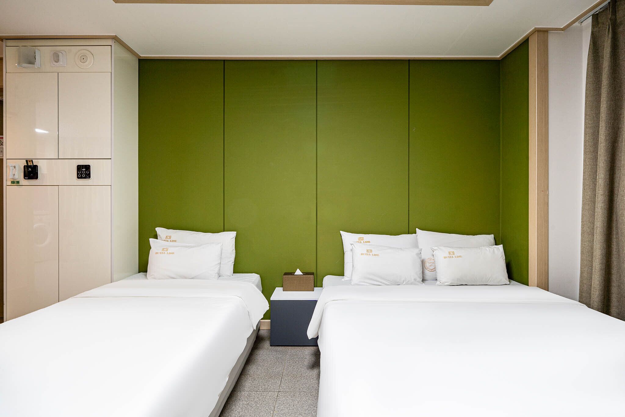 Ett hotellrum med två sängar, en grön accentvägg, en minibar och en garderob.