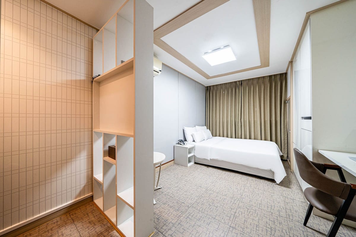 Une chambre d’hôtel comprenant un lit, une table de chevet, une chaise et un bureau avec une autre chaise.