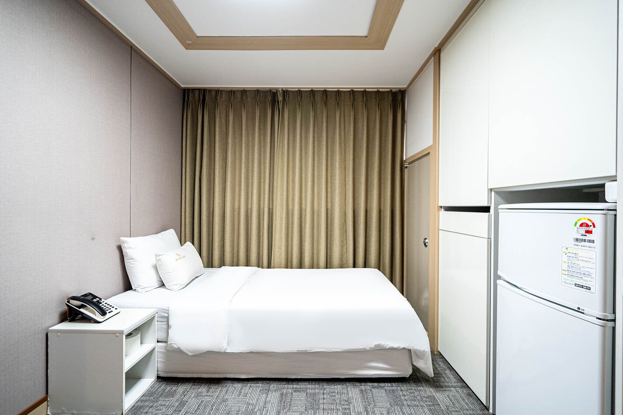 Habitación de hotel con cama, escritorio con teléfono, refrigerador y cortina.