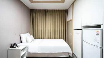 A hotel room with a bed, a desk with a phone, a refrigerator, and a curtain.