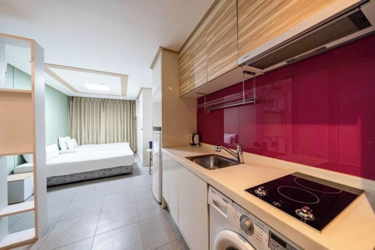 Una habitación de hotel compacta con kitchenette, una cama con vistas y lavadora.