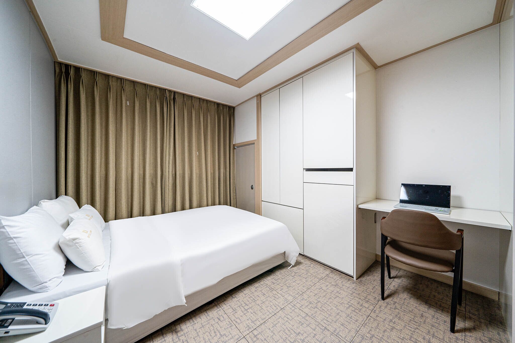 A hotel room with a bed, a desk with a laptop, and a wardrobe.