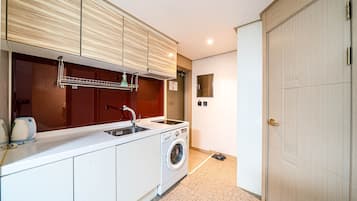 Une cuisine compacte avec des meubles blancs, un lave-linge encastré, un évier et une petite fenêtre.