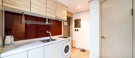 Una cocina compacta con armarios blancos, lavadora integrada, un lavabo y un ventanal pequeño.