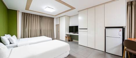 A hotel room with two beds, a kitchenette, a TV, and a refrigerator.