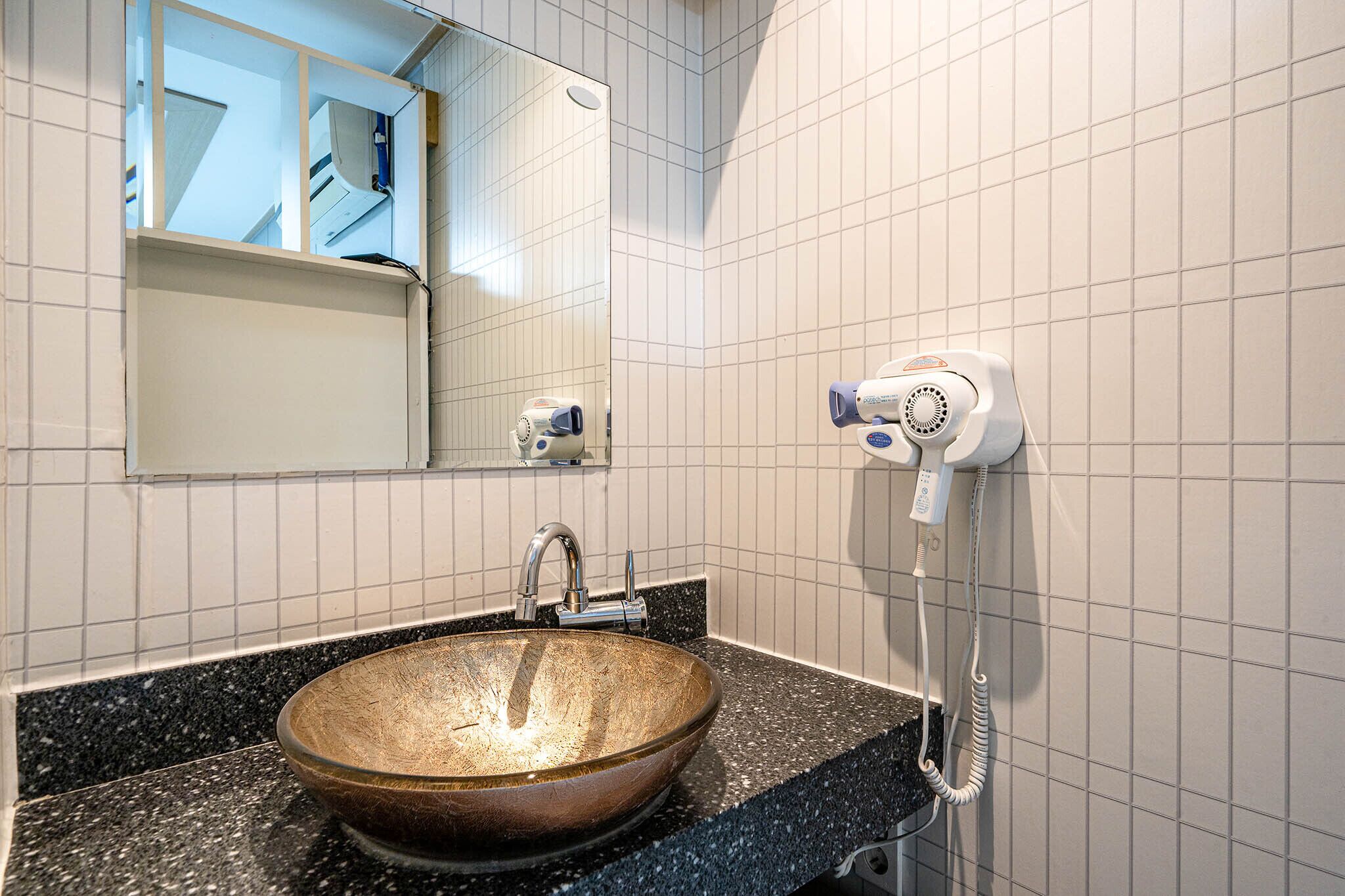 A bathroom with a large mirror, a sink with a vessel basin, and a hairdryer mounted on the wall.