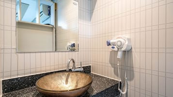 A bathroom with a large mirror, a sink with a vessel basin, and a hairdryer mounted on the wall.