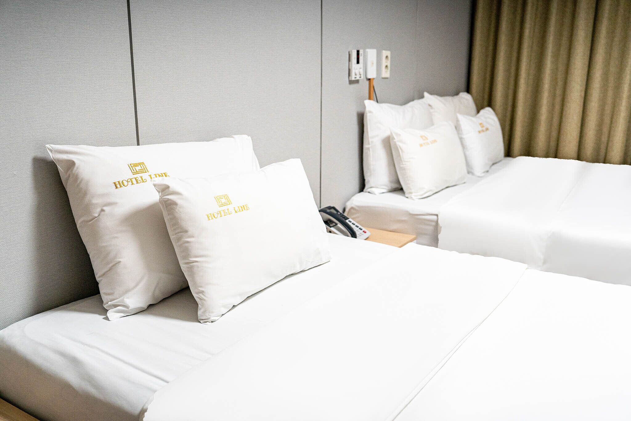 Een hotelkamer met twee bedden, elk voorzien van witte beddengoed en kussens met het logo van het hotel.
