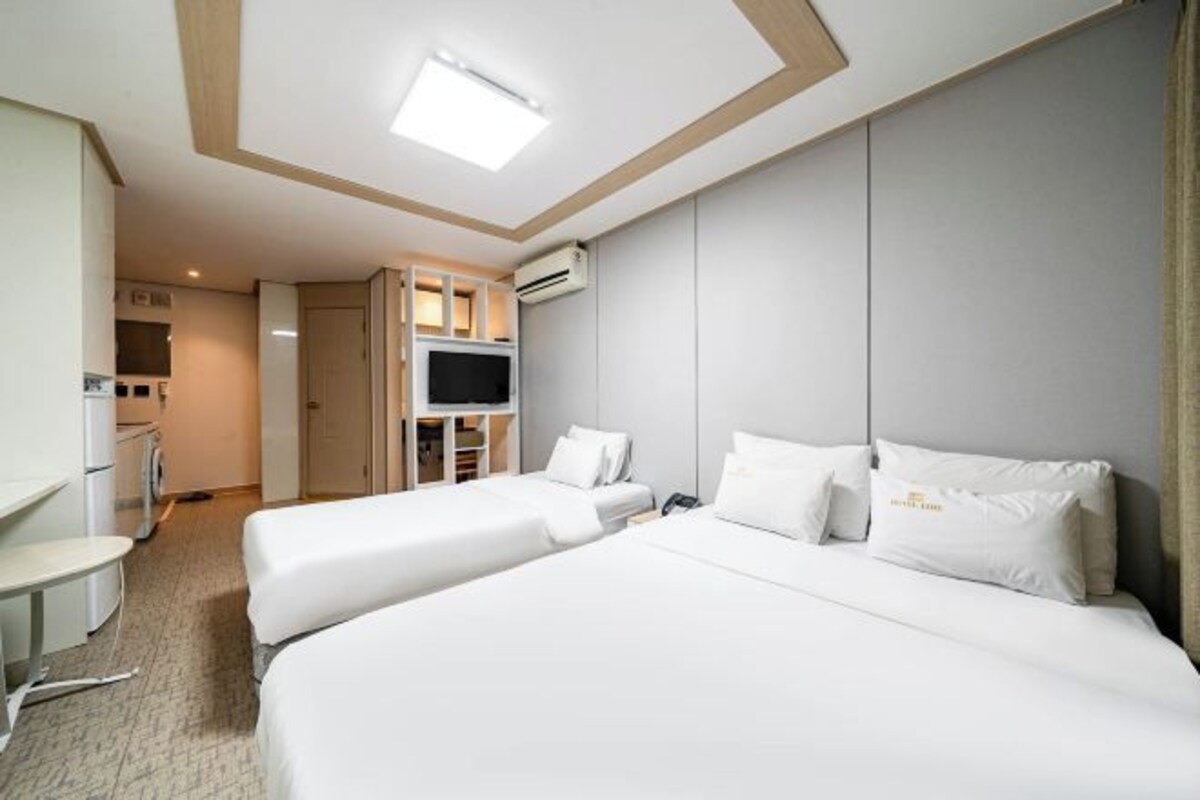 Habitación de hotel con dos camas, televisión, escritorio y kitchenette.