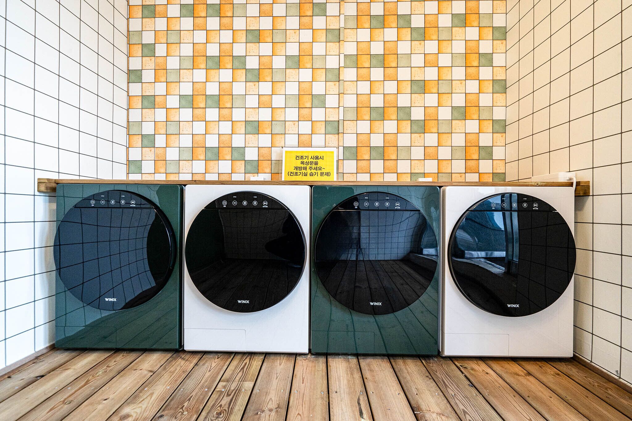 A row of four front-loading washing machines with a tiled backsplash above them.