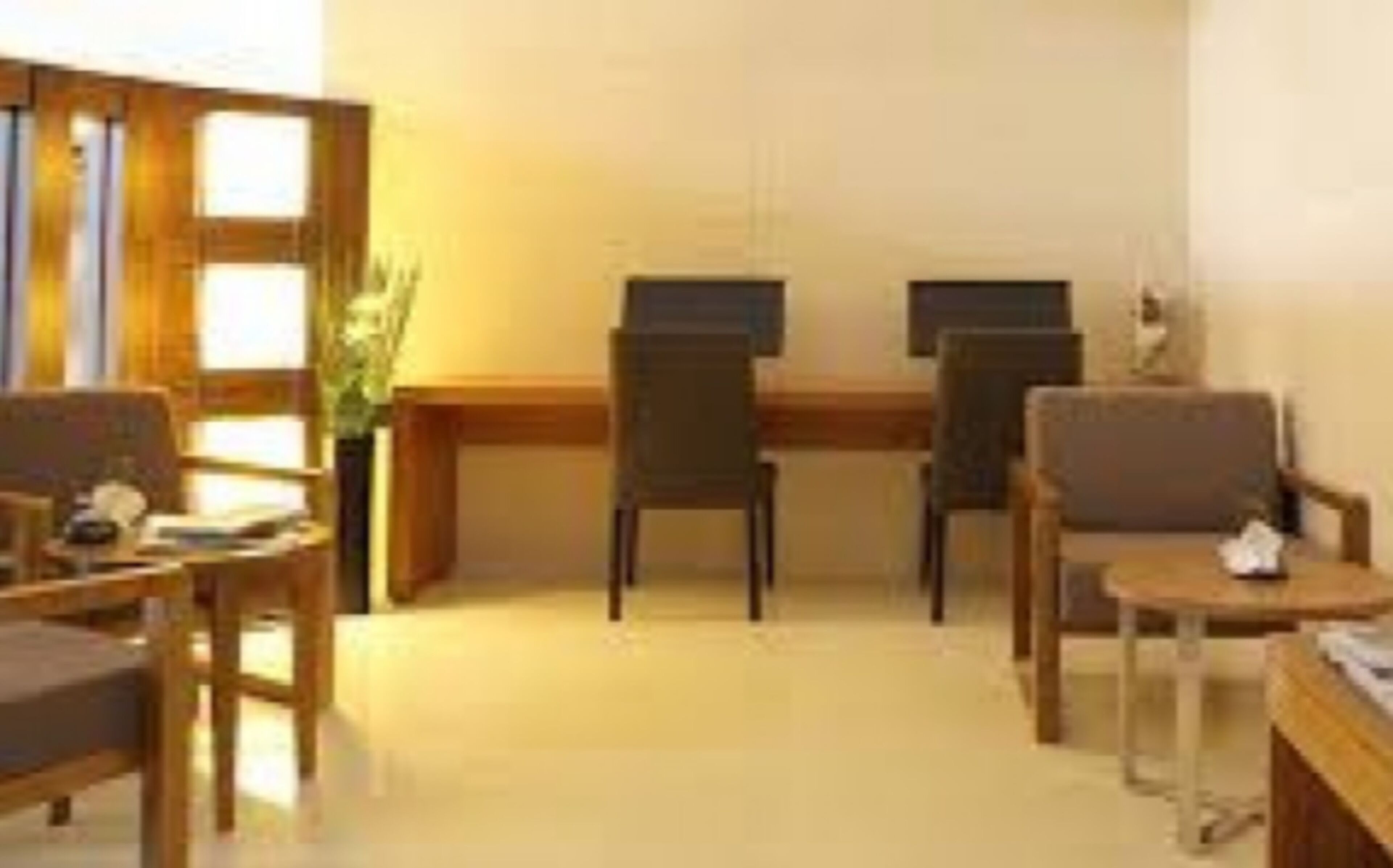 A room with a wooden desk, two chairs, a small table, and a plant.