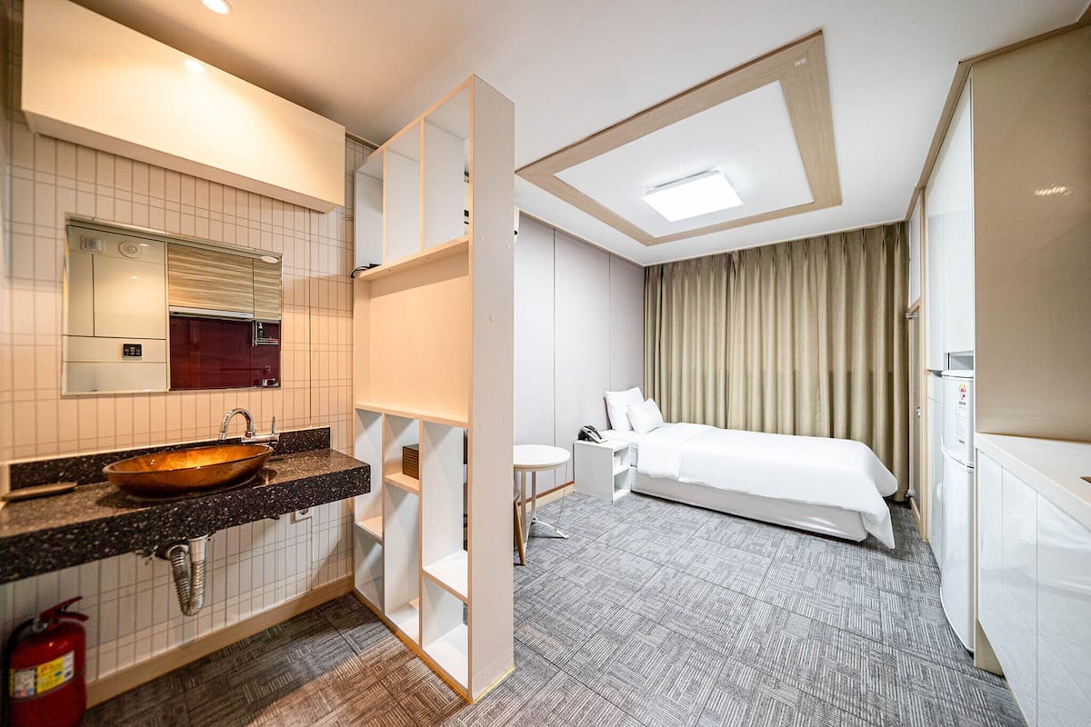 Une chambre d’hôtel avec un grand lit, une salle de bain avec un lavabo et un miroir, et une petite table.