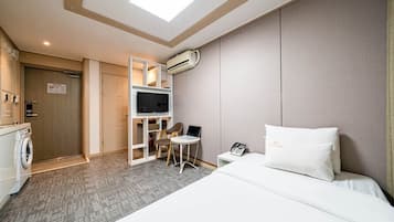 Habitación de hotel con cama, escritorio con silla, televisor, lavadora y aire acondicionado.
