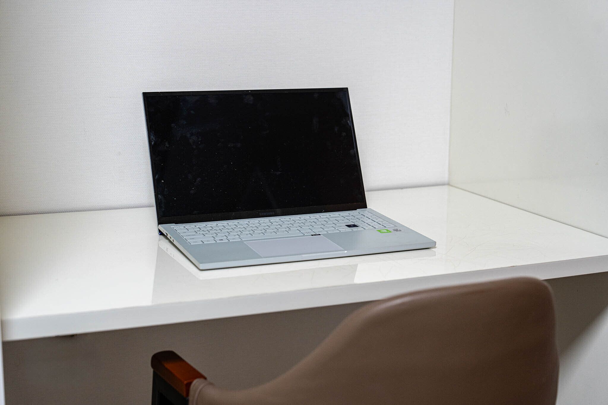 Ein Laptop auf einem weißen Schreibtisch mit einem Stuhl davor.
