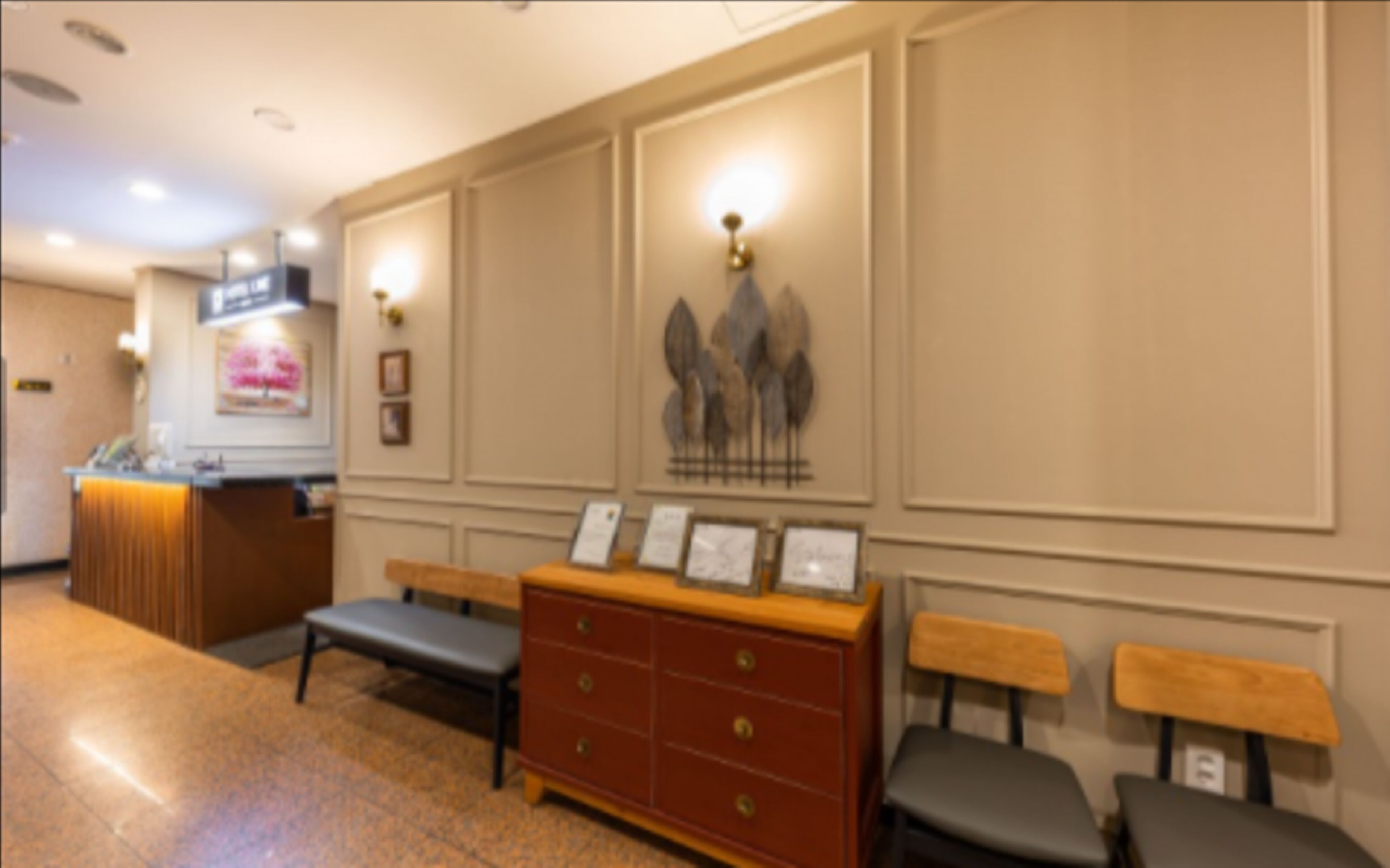 A reception area with a counter, a bench, a wooden cabinet with drawers, and wall-mounted light fixtures.