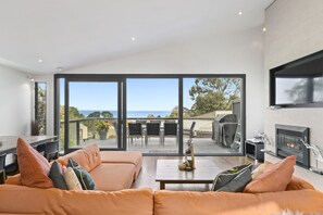 A modern living room with a large sliding glass door leading to an outdoor patio with a view of the sea.