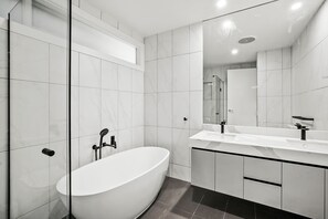 A modern bathroom with a freestanding bathtub, a large mirror, and a vanity with a sink. - Breakers 4 (Lorne)