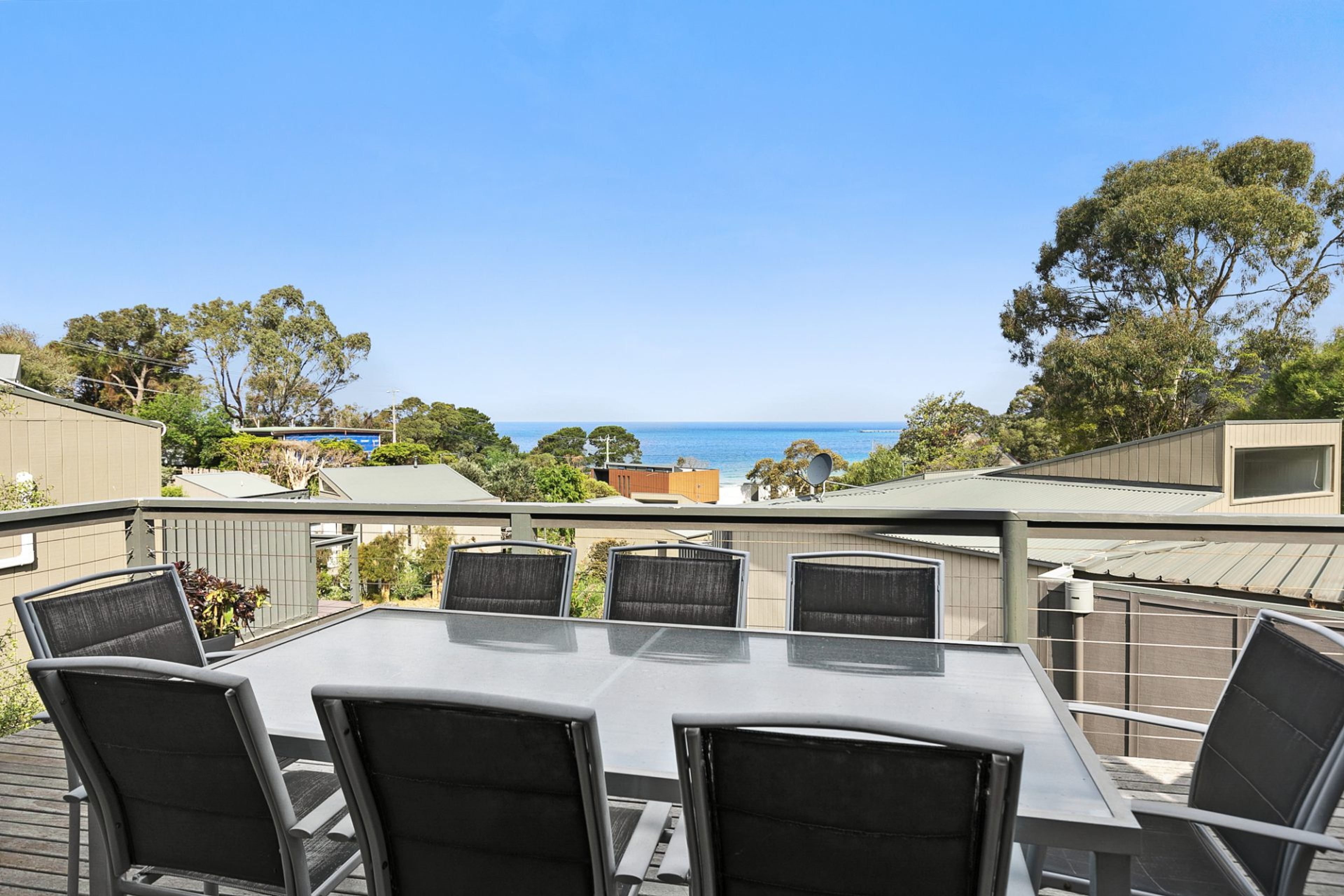An outdoor patio with a table and chairs, overlooking a body of water and trees.