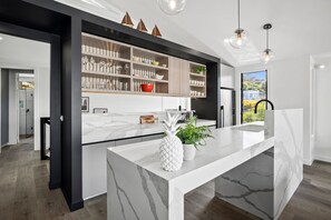 A modern kitchen with a marble countertop, built-in shelves, and pendant lighting.