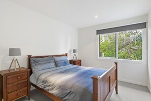 Une chambre à coucher avec un lit en bois, deux tables de chevet avec des lampes, une fenêtre donnant sur un paysage verdoyant et un mur blanc.
